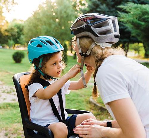 foto de un niño en el asiento trasero de una 自行车 que ayuda a su madre a abrocharse el 头盔